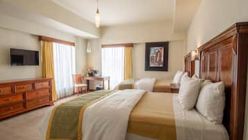 A hotel room with two beds, a desk, a chair, a TV, and a painting on the wall.