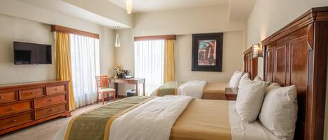 A hotel room with two beds, a desk, a chair, a TV, and a painting on the wall.