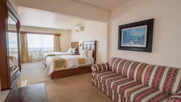 A hotel room with two beds, a sofa, a wooden bench, and a framed picture on the wall.