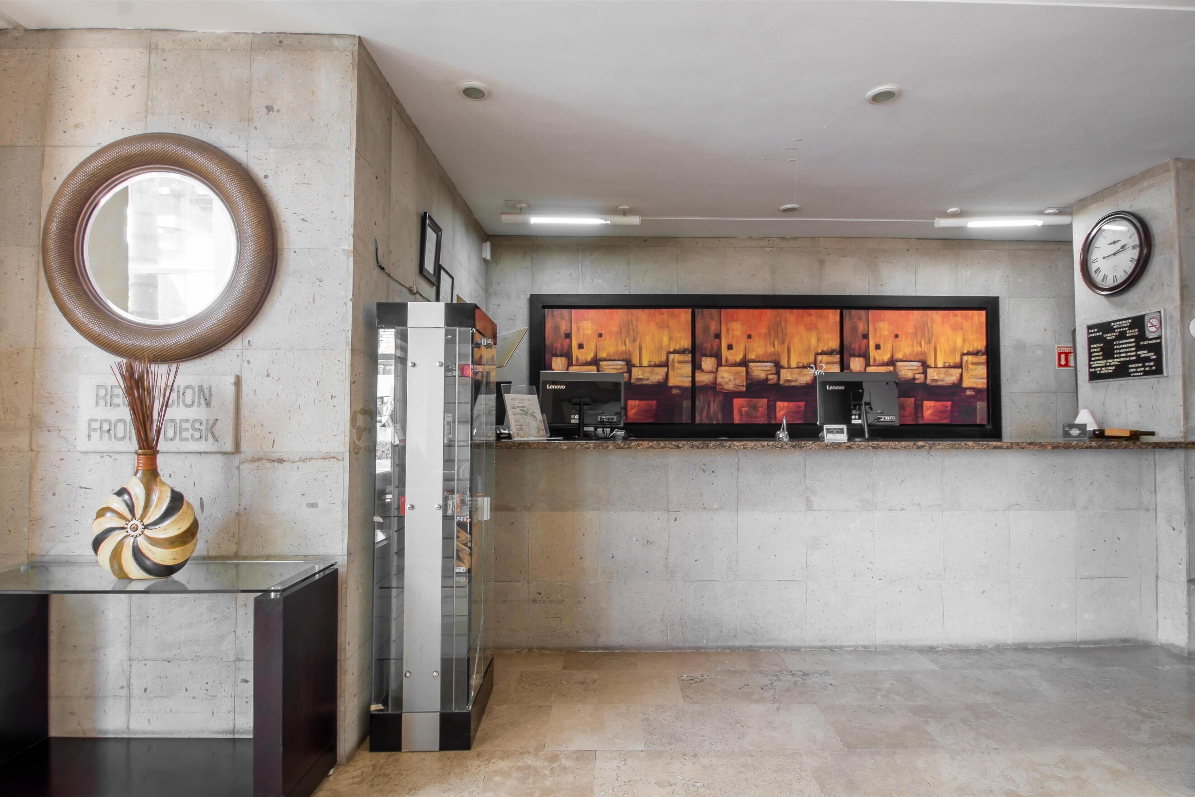 Un área de recepción con diseño moderno, que presenta un espejo redondo, un jarrón decorativo, una máquina de café y un cuadro abstracto de gran tamaño en la pared.