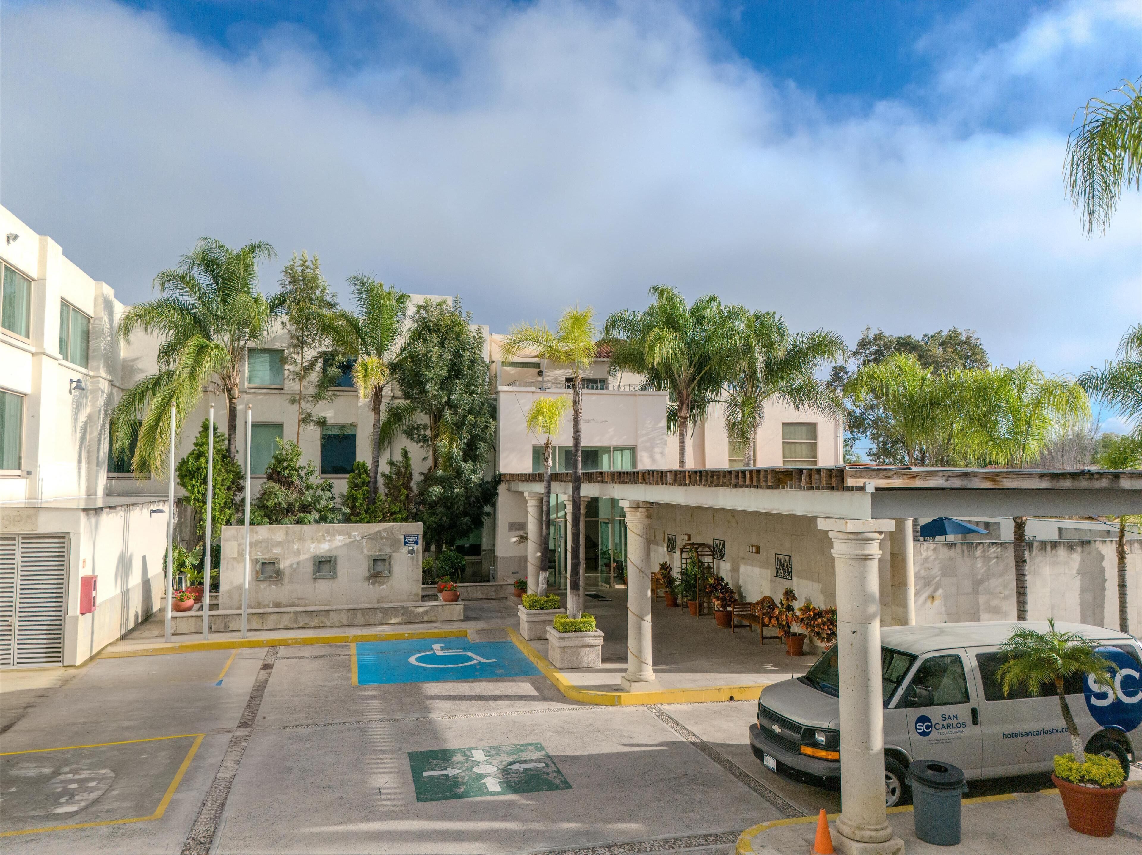 A hotel entrance with a disabled parking space, a van, and a covered outdoor seating area.