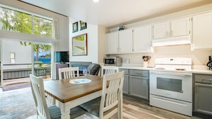 A modern kitchen with white cabinetry, a dining area with a wooden table and white chairs, and a view of the sea through large windows. - JL 202: Lovely water view (Blaine)