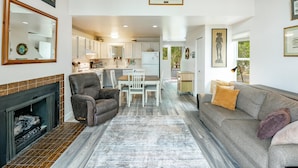 A spacious living area with a fireplace, a grey sofa, a dining table with chairs, and a kitchen in the background. - JL 202: Lovely water view (Blaine)