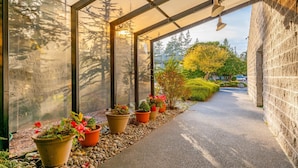 A covered walkway with potted plants and a view of trees and a car in the background. - JL 202: Lovely water view (Blaine)