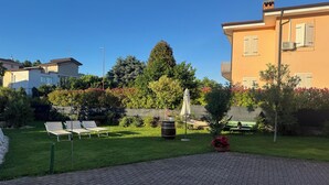 A courtyard with a paved walkway, lounge chairs, a hammock, and a small garden area with potted plants and flowers. - House with private pool x families and companies (Caprino veronese)
