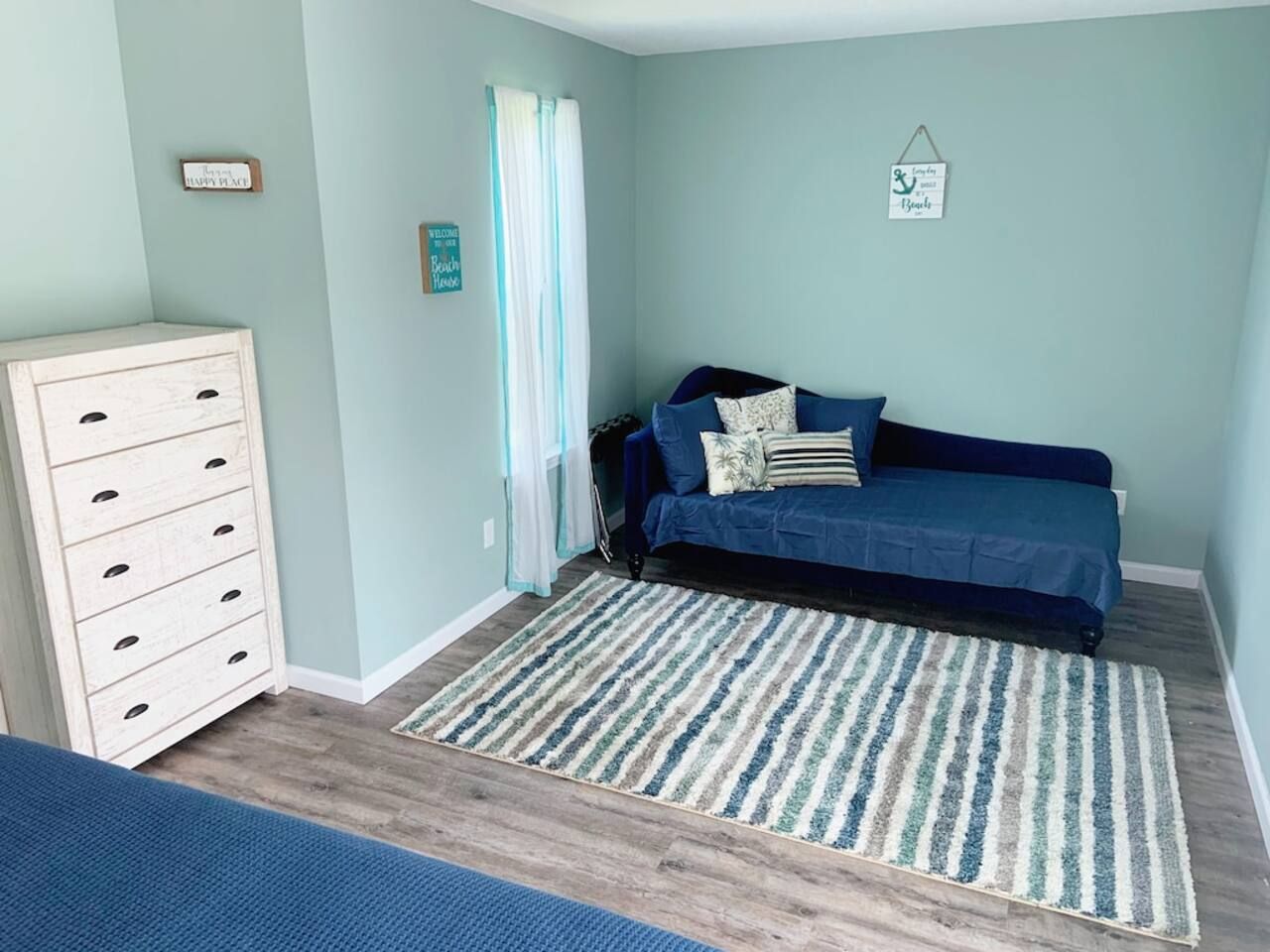 A room with a blue sofa, a wooden dresser, a striped rug, and a wall with a welcome sign.