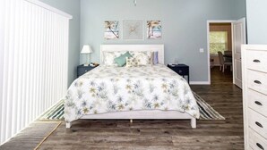 Quarto com cama, mesa de cabeceira, cômoda, ventilador de teto e obras de arte na parede.