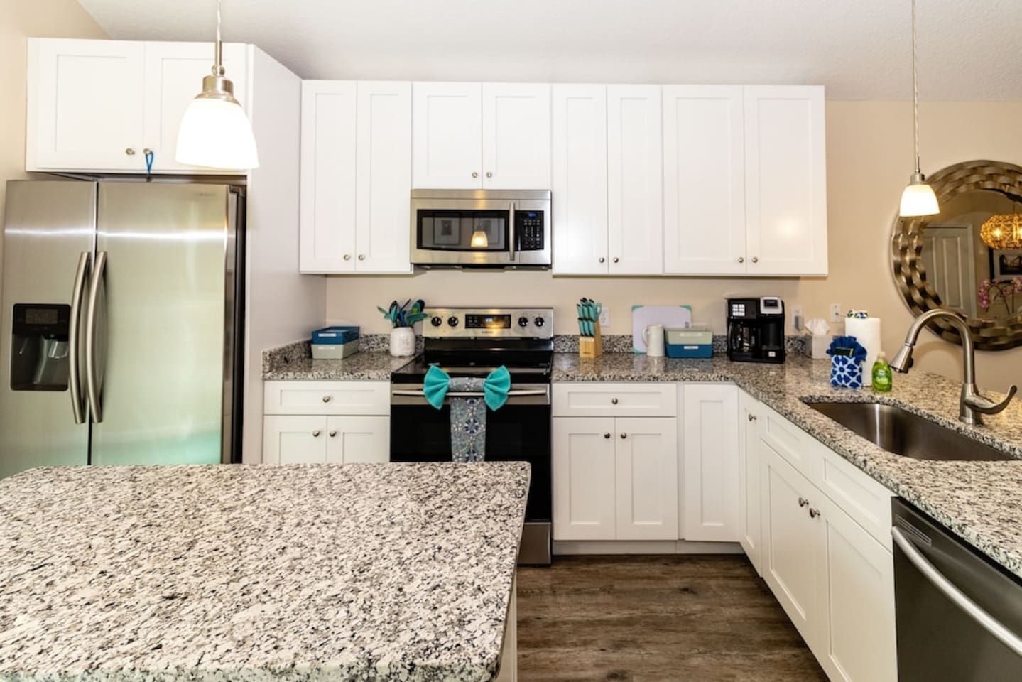 A modern kitchen with white cabinets, granite countertops, stainless steel appliances, and a decorative bow on the oven handle.