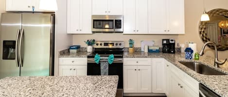 Una cocina moderna con armarios blancos, encimeras de granito, electrodomésticos de acero inoxidable y un lazo decorativo en el pomo del horno.
