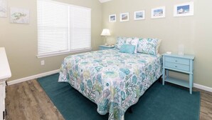 A bedroom with a bed, a nightstand, a window with blinds, and wall art. - Beach Haven (saint augustine)