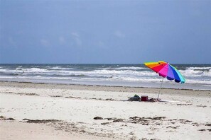 Una playa con un paraguas colorido y una hielera en la arena.