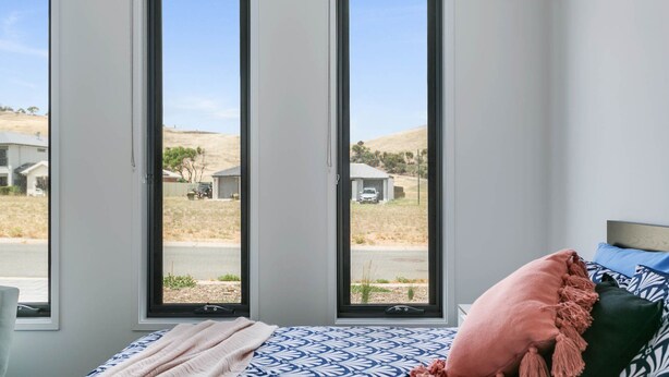A bedroom with a large window, a bed with patterned bedding, and a view of a residential area.
