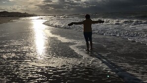 Une personne se tient sur une plage, les bras tendus, face à l’océan.