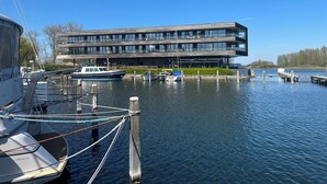 Un bâtiment moderne à étages, des bateaux amarrés et une étendue d’eau calme.