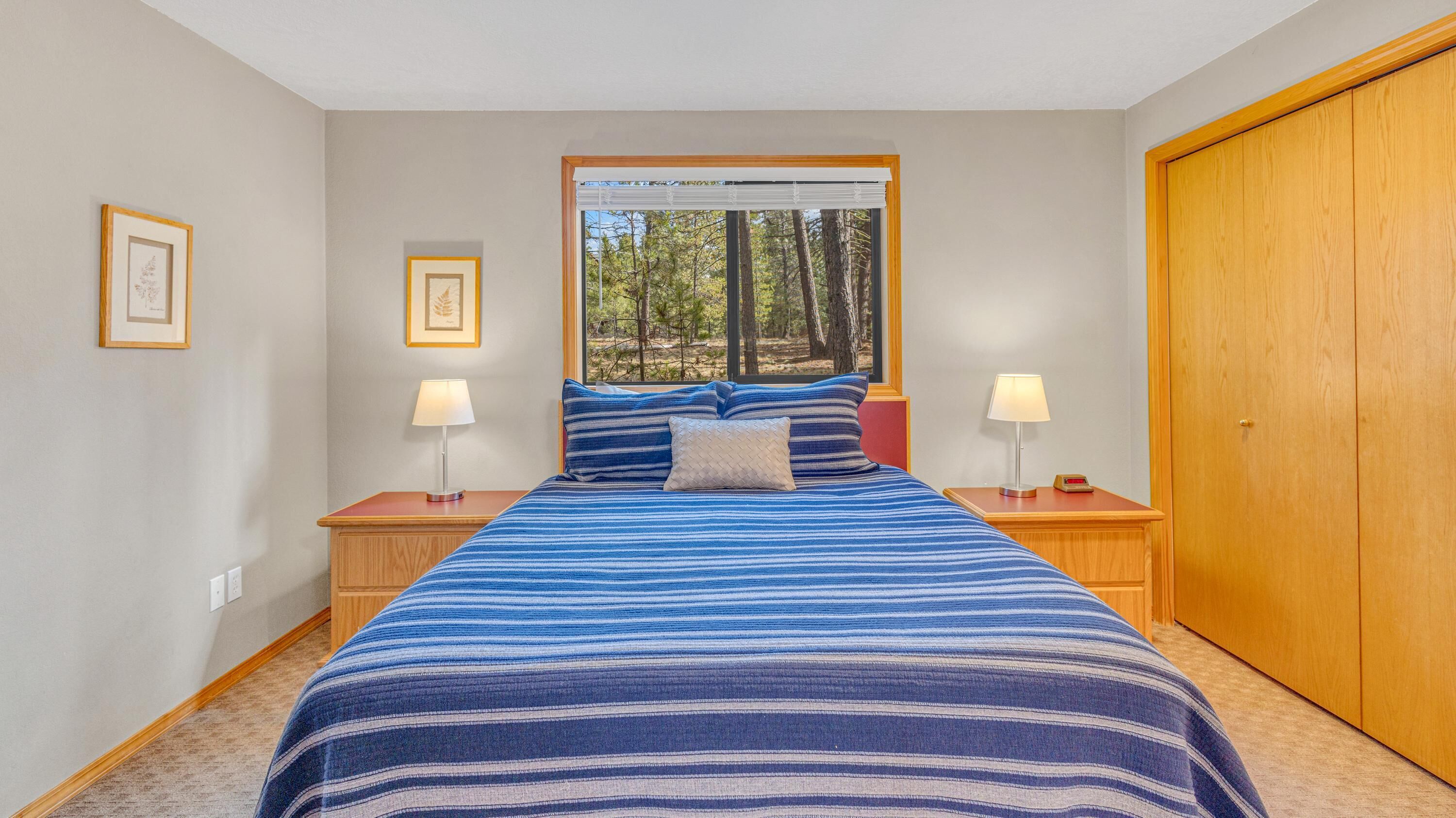 Une chambre avec un grand lit, deux tables de chevet avec des lampes, une fenêtre donnant sur une forêt et une armoire en bois.