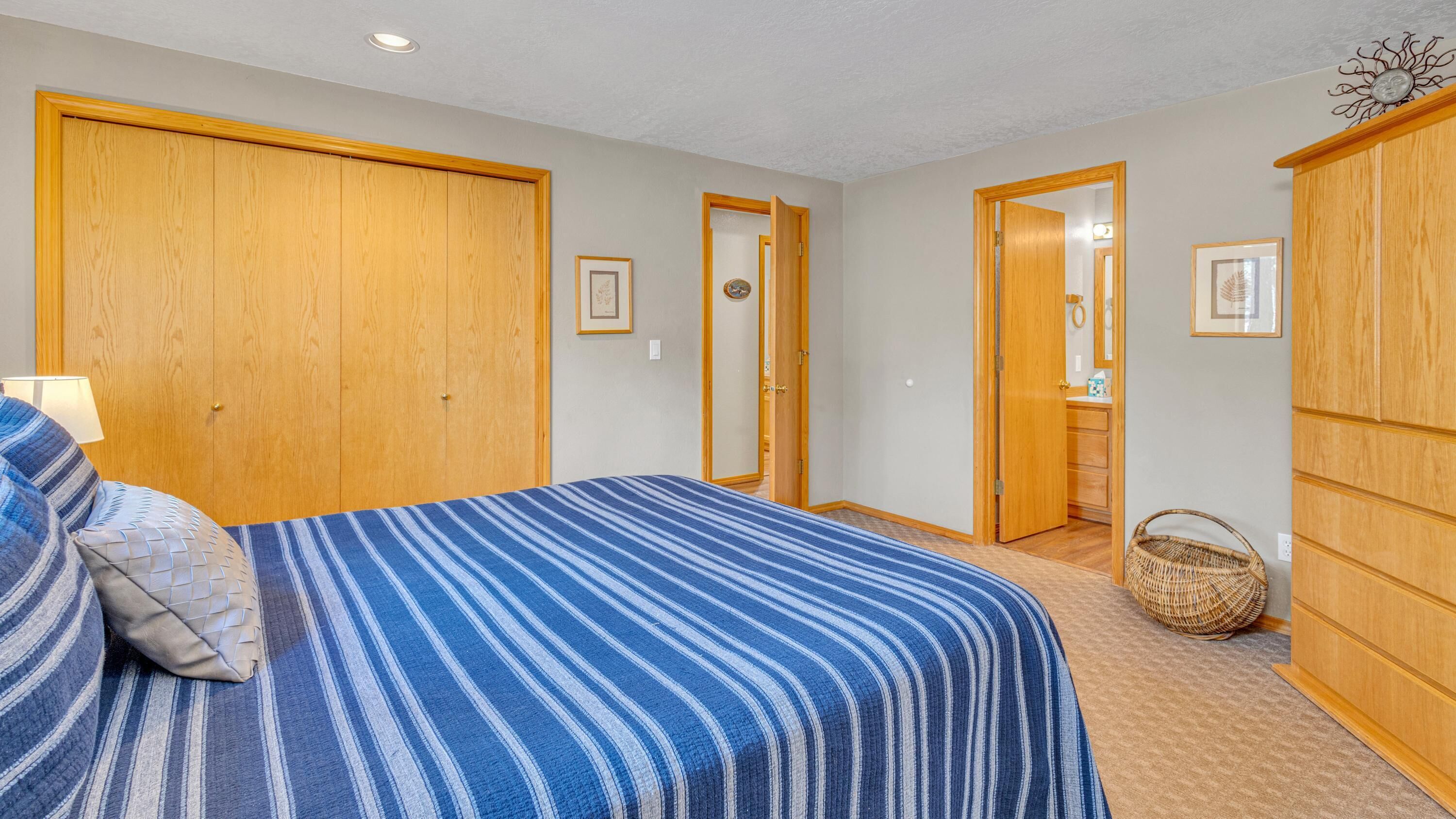 A bedroom with a bed, wooden wardrobe, and a bathroom visible through an open door.