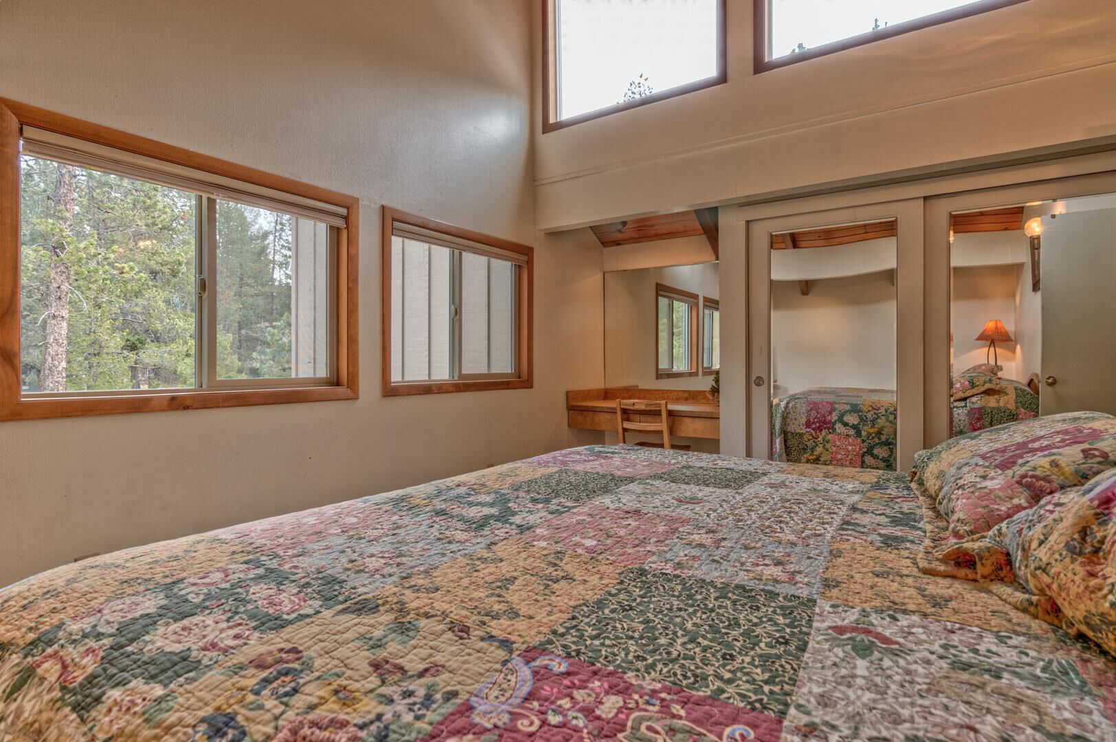 A bedroom with a large bed, a desk, and a chair. There are windows and a door leading to another room.