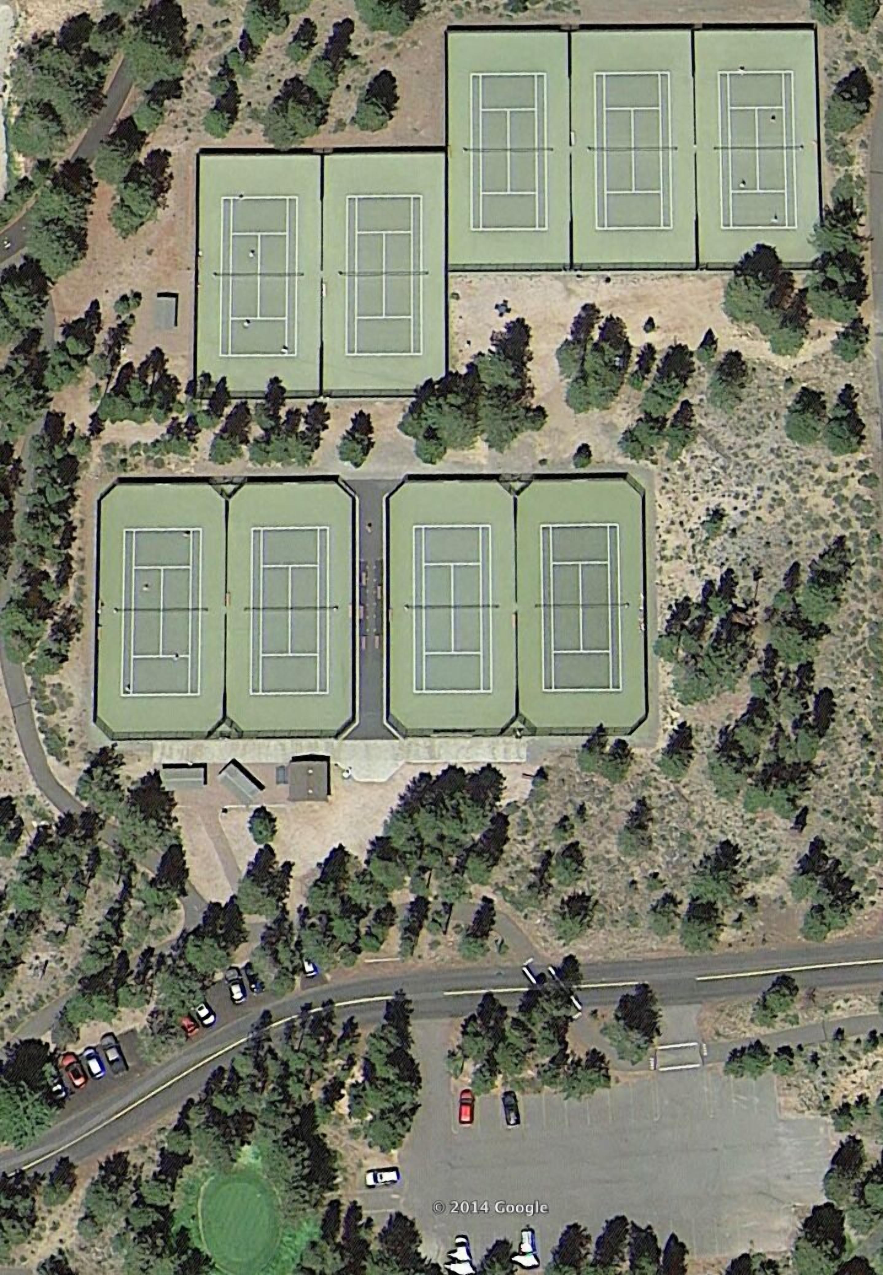 An aerial view of a sports complex with multiple tennis courts, parking areas, and surrounding greenery.