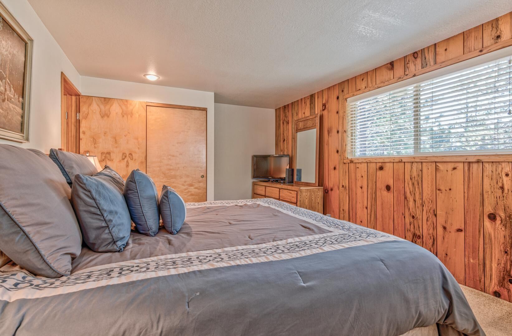 A bedroom with a large bed, wooden walls, a television, and a window with blinds.