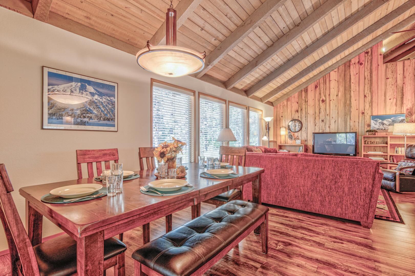 A dining area with a wooden table set for four, a bench, and a red upholstered sofa in the background.