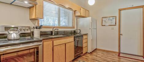 Una cocina con gabinetes de madera, estufa, refrigerador y ventana con persianas.