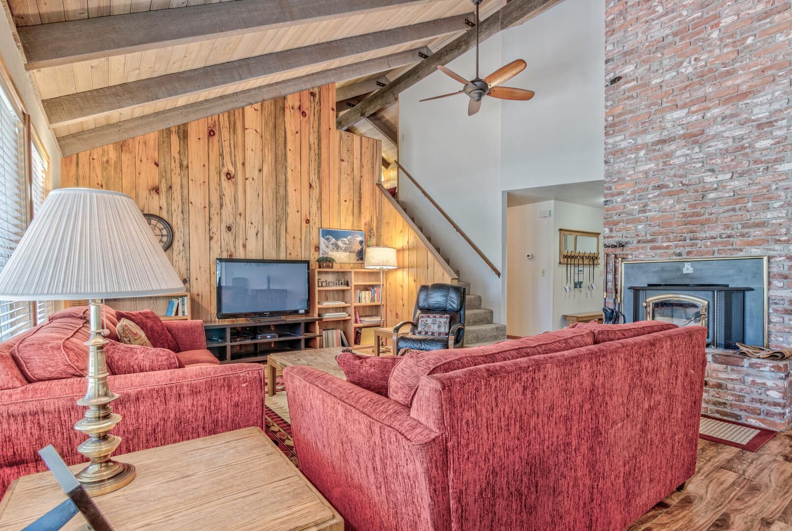 Un salón acogedor con pared de madera, chimenea, televisor y muebles tapizados en rojo.