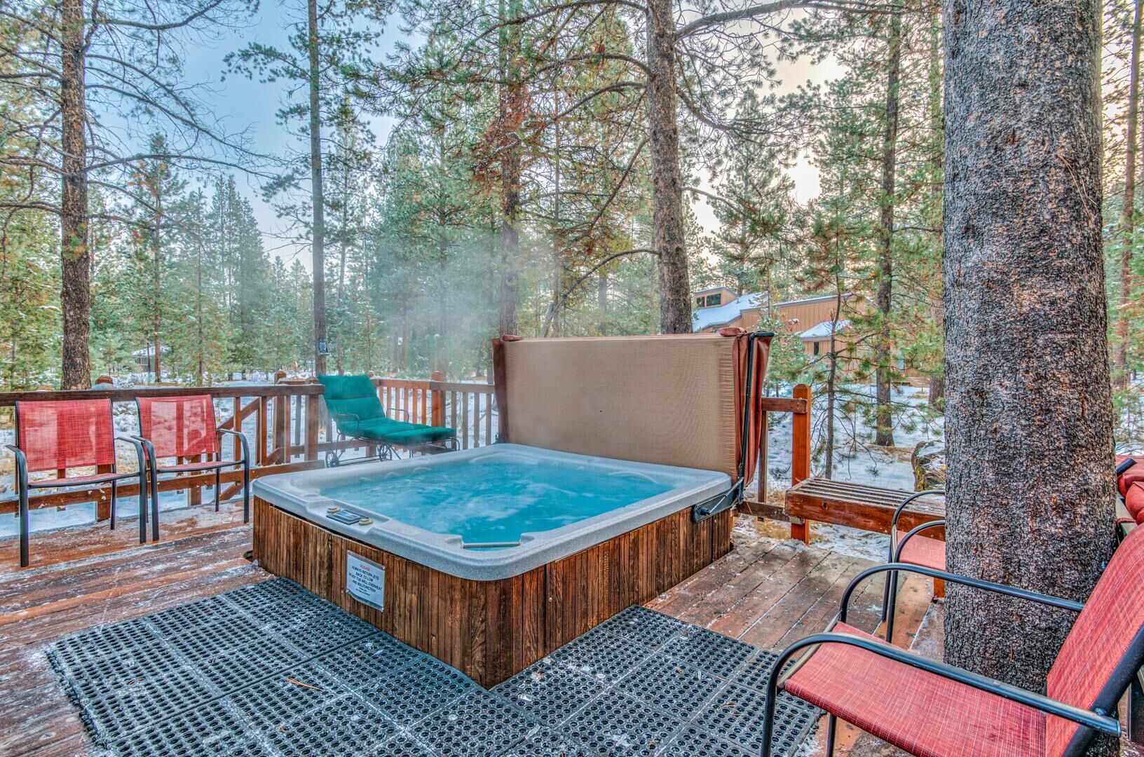 Un bain à remous sur une terrasse en bois, entouré d’arbres, avec des chaises et un espace abrité.