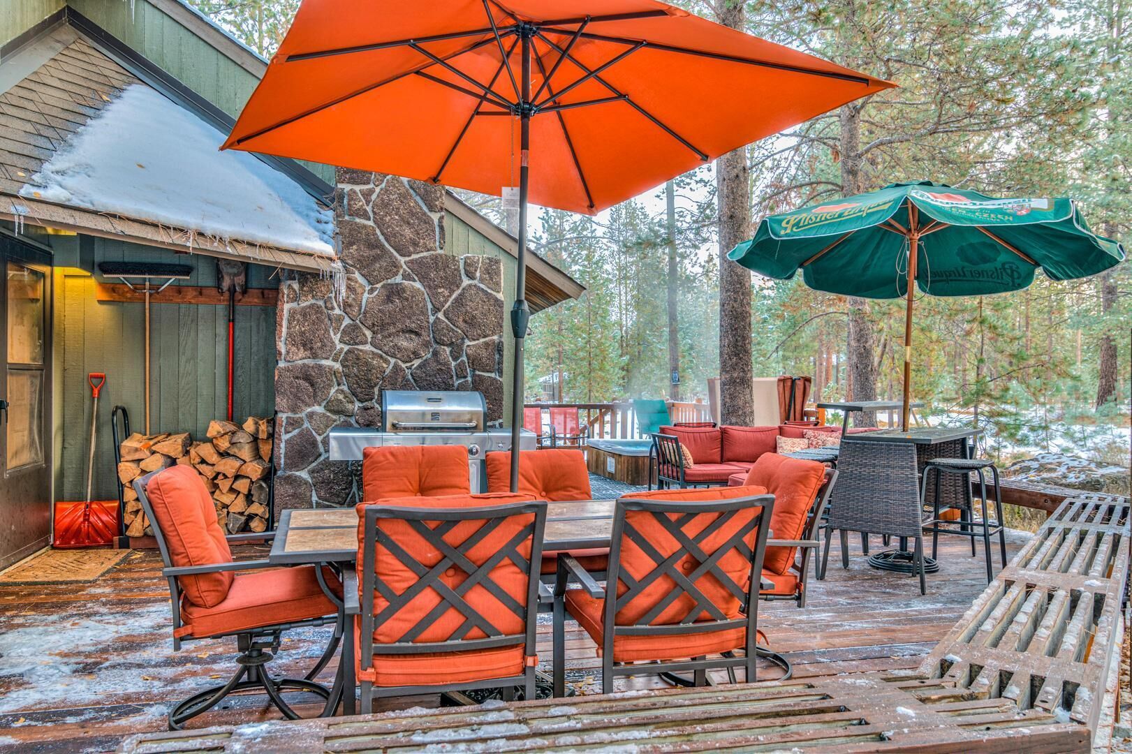 An outdoor patio with a stone fireplace, orange and green umbrellas, and a variety of seating options.