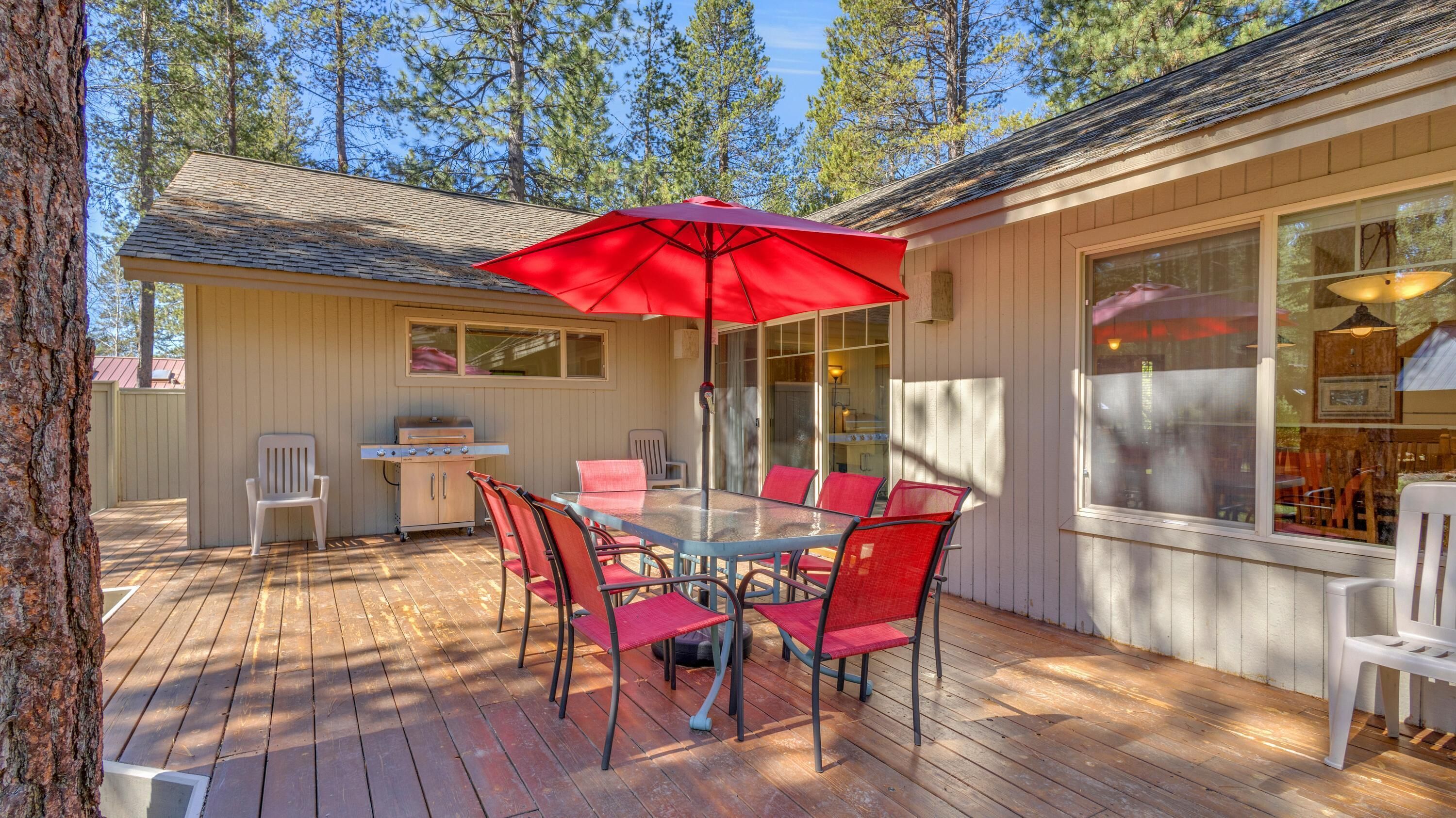Un terrazzo in legno con tavolo e sedie, un barbecue e un'ampia finestra.