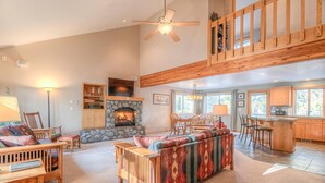 A spacious living room with a stone fireplace, wooden furniture, and a dining area with natural light. - Awbrey Lane 2 (Bend)