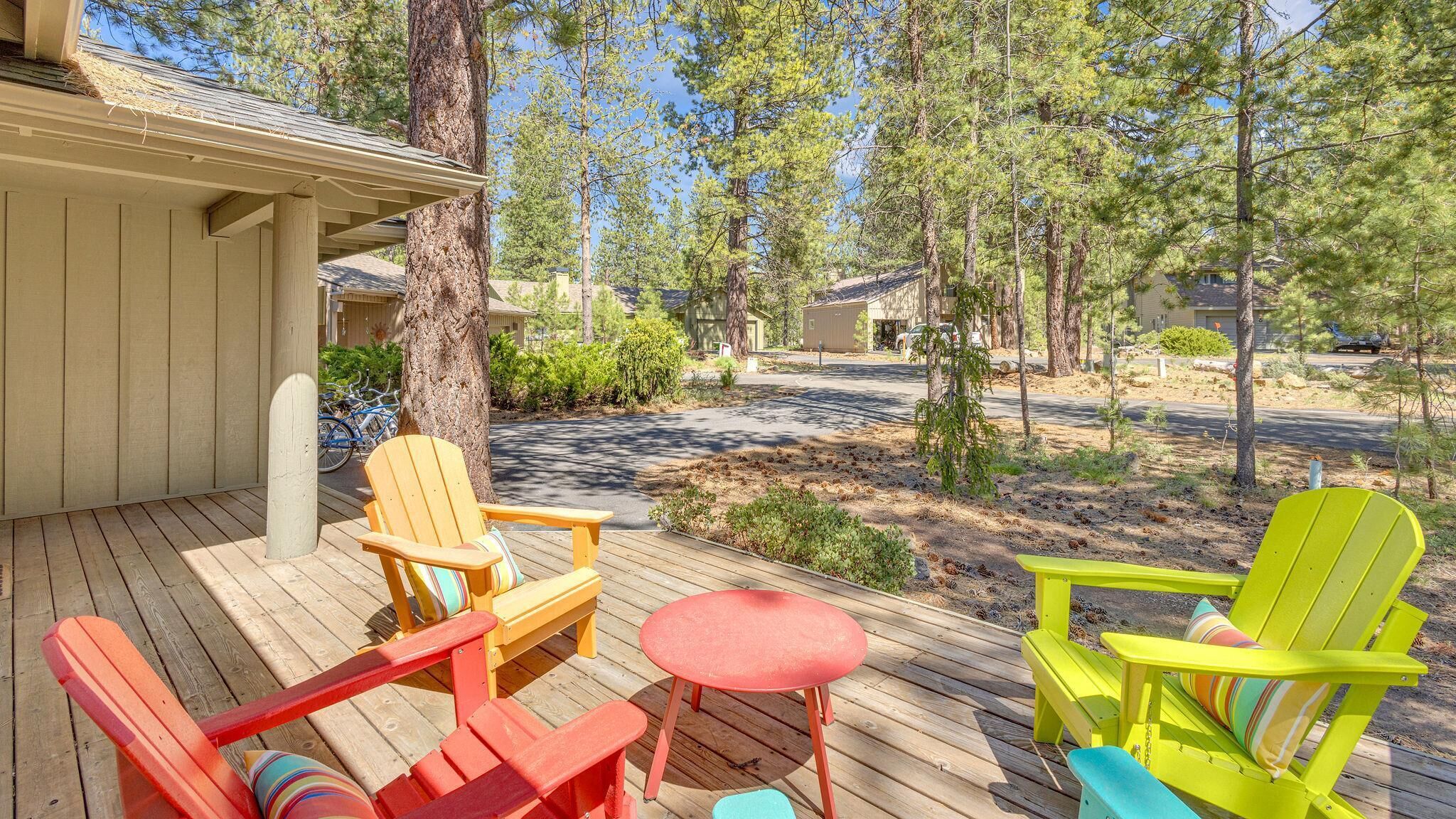 Un terrazza in legno con poltrone Adirondack colorate e un tavolino rotondo.