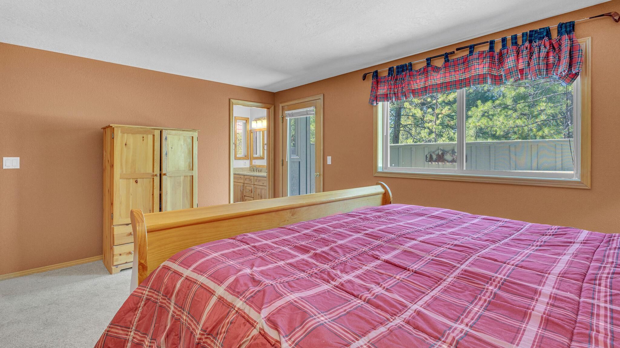A bedroom with a bed, a wardrobe, a mirror, and a window with a view of trees.
