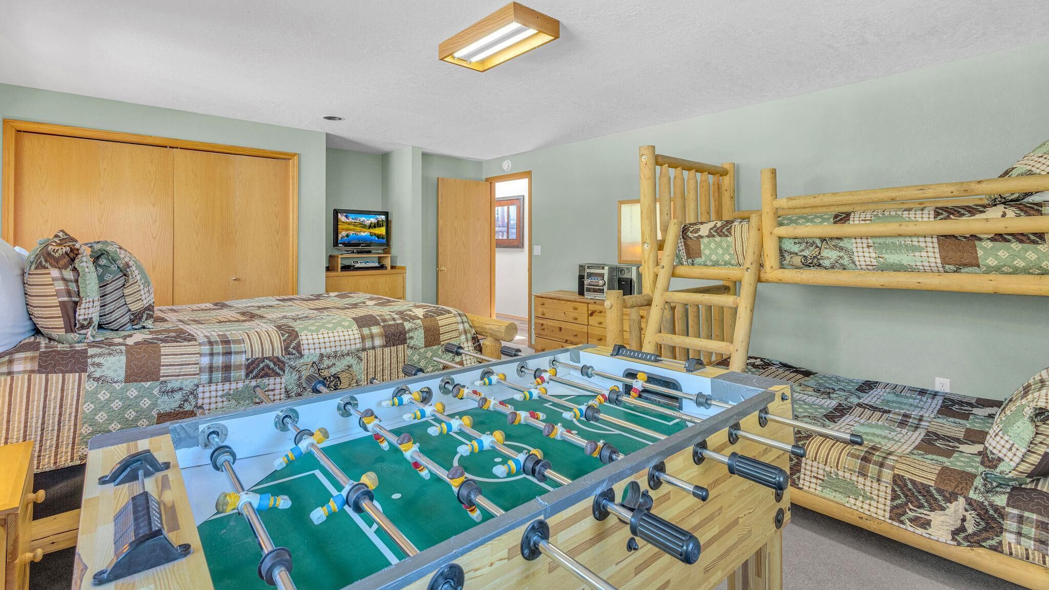 A room with a foosball table, bunk beds, a television, and a wooden cabinet.