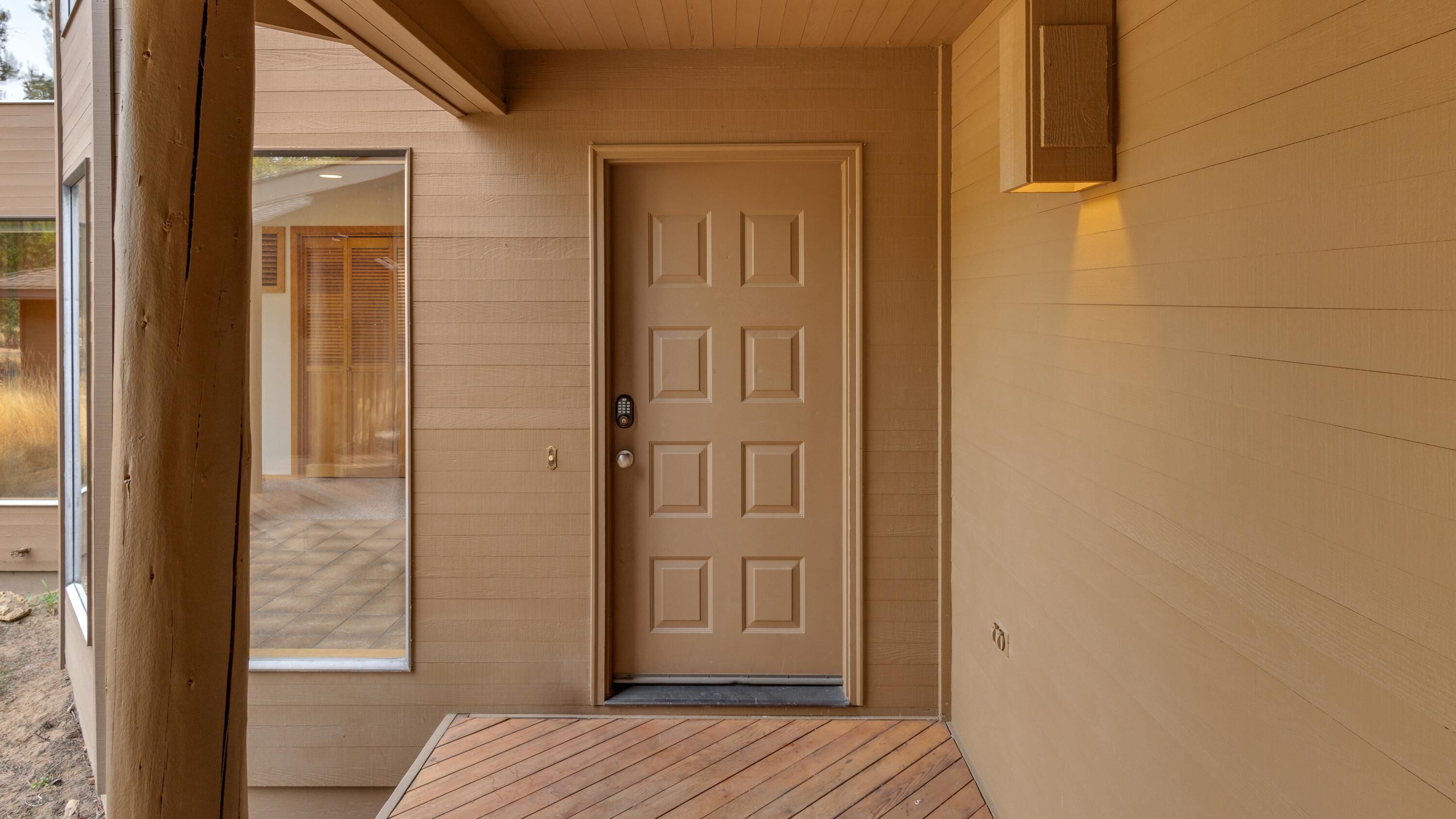 A wooden door with a keypad lock, a small step leading up to the door, and a wooden wall with a light fixture above it.