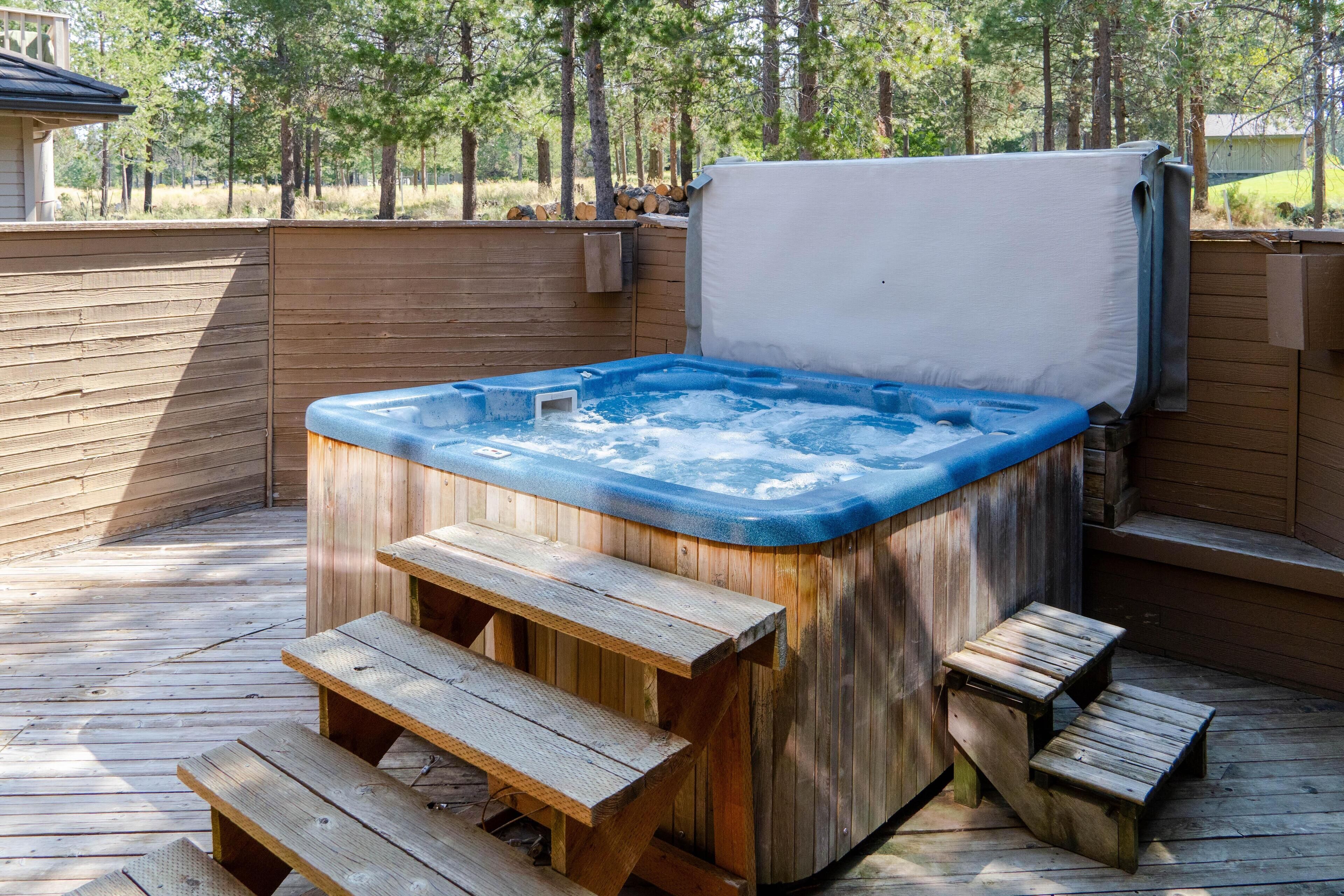 Ein hölzernes Whirlbad mit Stufen, umgeben von einer Holzterrasse und einem Holenzaun.