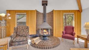 A cozy room with a wood-burning stove, two patterned chairs, a small table, and a lamp.