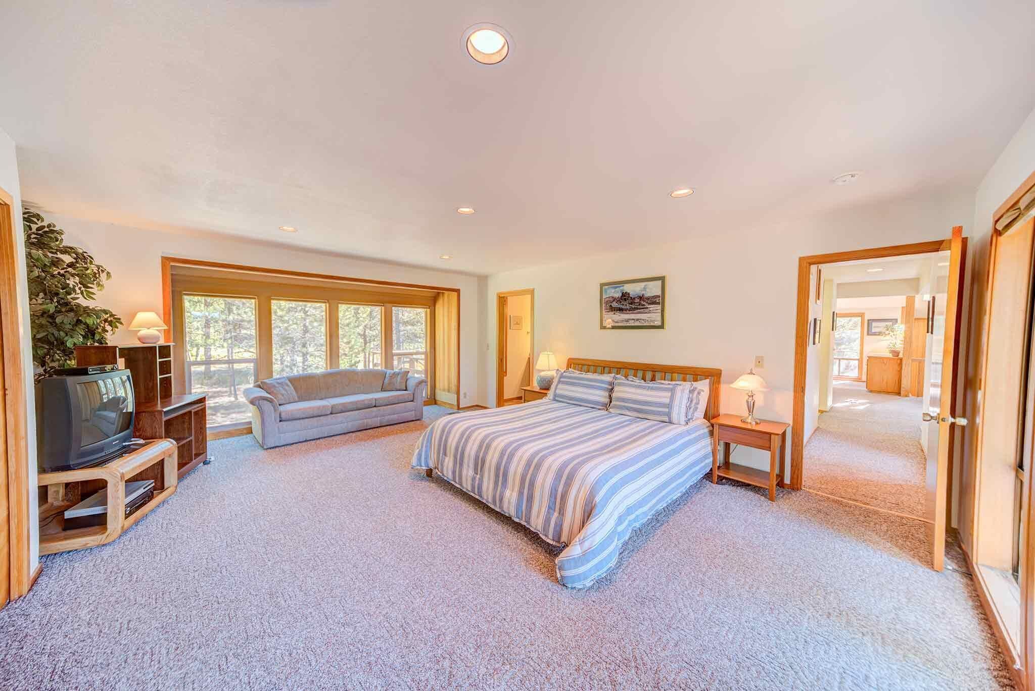 A spacious bedroom with a large bed, a sofa, a TV, and a window.