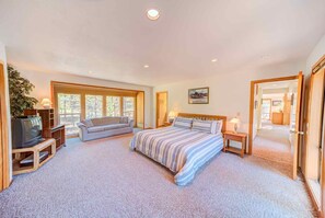 A spacious bedroom with a large bed, a sofa, a TV, and a window.