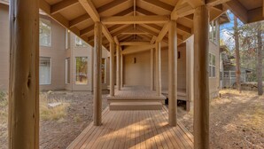 A covered wooden deck with a simple, open design, surrounded by a building with large windows and a natural landscape.