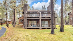 A multi-story log cabin with a balcony, surrounded by tall trees and a clear sky. - Wildflower Condo 54 (Bend)