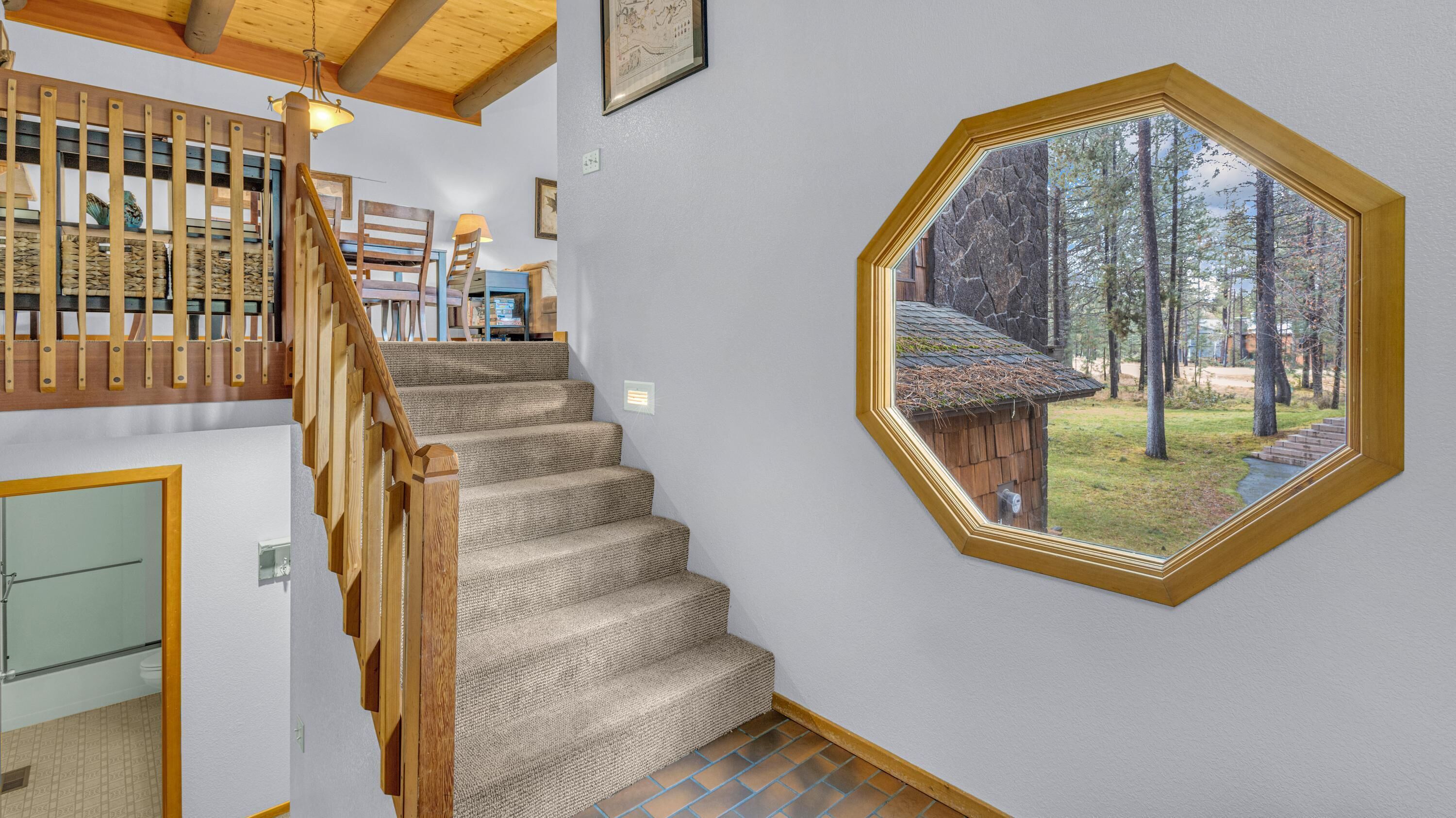 A staircase with a wooden railing leading to a room with a large octagonal window overlooking a forest.
