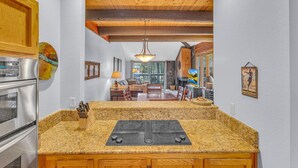 A kitchen with granite countertops, a built-in stove, wooden cabinets, and a dining area with a table and chairs. - Wildflower Condo 54 (Bend)