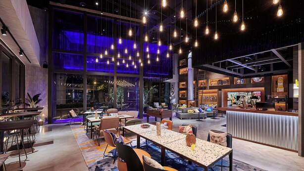 A modern hotel lobby with a seating area, a reception desk, and a large window overlooking the city.