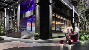 A modern building with a glass facade, a staircase leading to an upper level, and a large spherical sculpture in the foreground.
