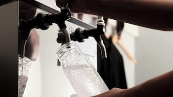 A hand filling a glass bottle with water from a tap.