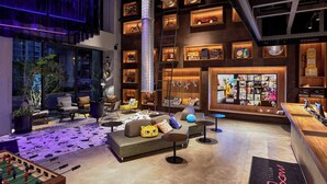 A modern lobby with a sofa, coffee table, and foosball table. There are shelves with various items and a reception desk.