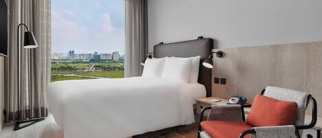 A hotel room with a large bed, a chair, a nightstand, and a view of a cityscape.