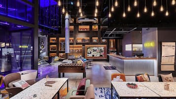 A modern indoor space with tables, chairs, a foosball table, and a bar area.