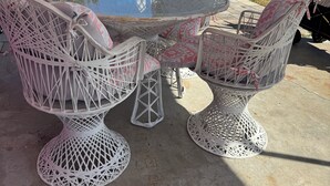 Een ronde, buiteneetset met rieten stoelen en een glazen tafel, geplaatst op een beton terras.