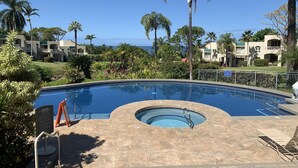 A swimming pool with a curved design, surrounded by palm trees and a view of the ocean. - Beautiful - Palms at Wailea 1802 (Kihei)
